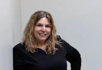 A woman in a black shirt is leaning against a wall and smiling.