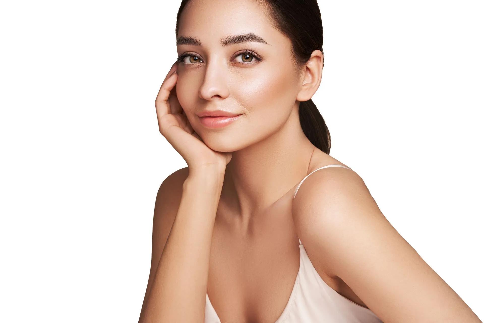 A woman with a hand on her face is smiling and looking at the camera.
