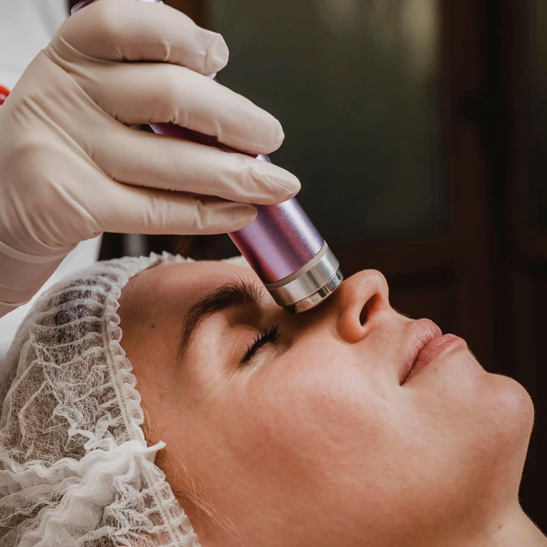 A woman is getting a facial treatment with a purple device on her face.