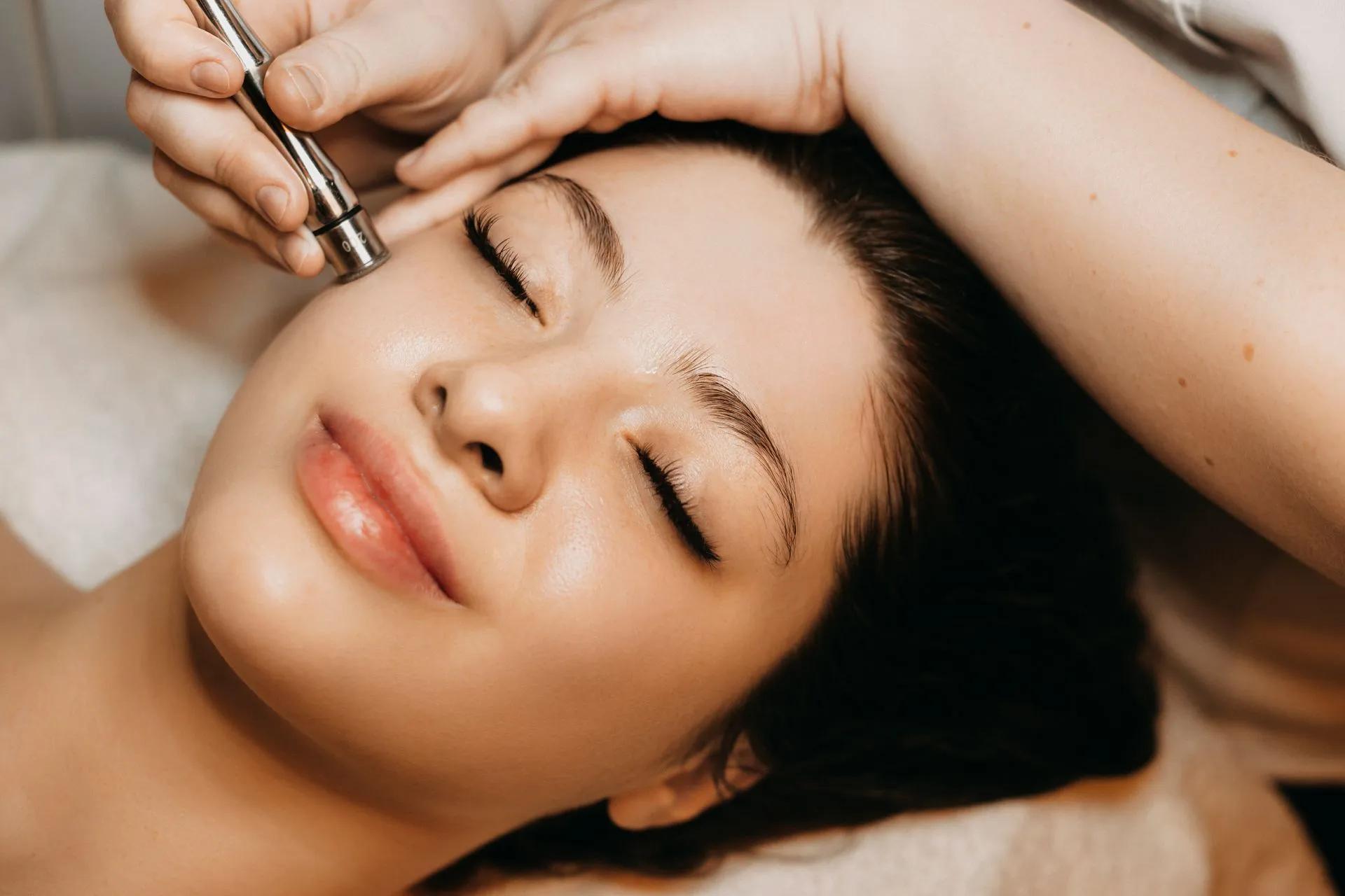 Woman receiving a microdermabrasion treatment on her face; eyes closed, spa setting.