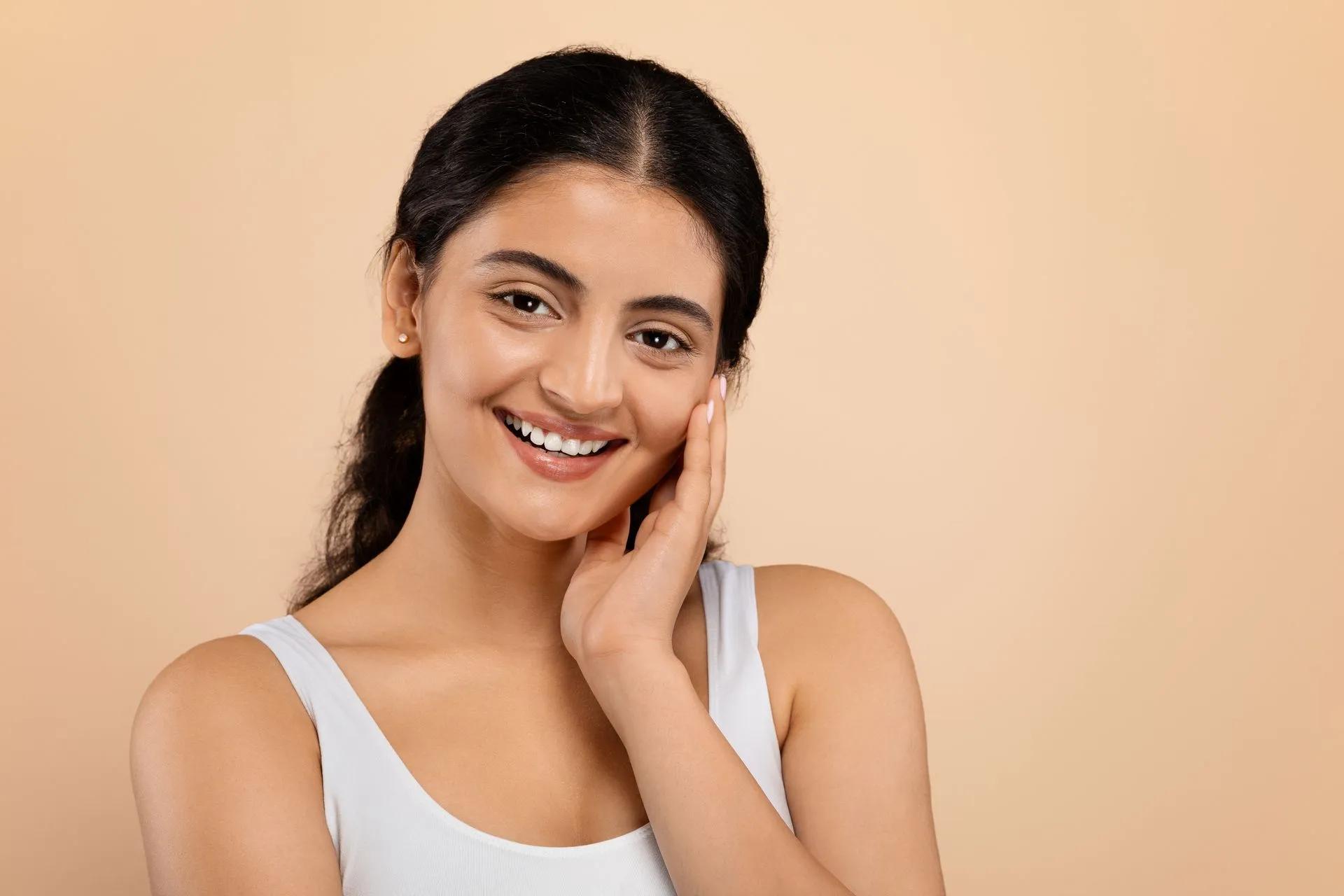 A woman is smiling and touching her face with her hand.